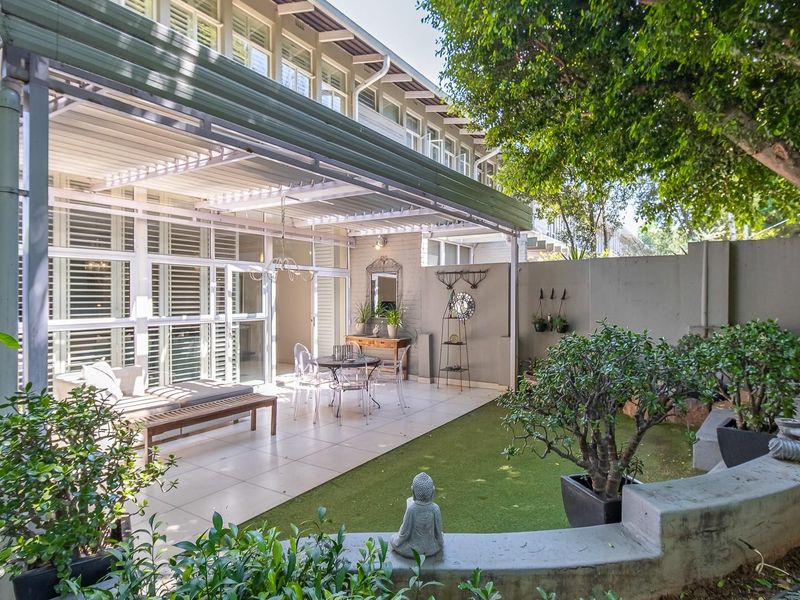 A well-maintained rear patio area featuring tiled flooring, a covered pergola structure, and a landscaped garden with a low concrete retaining wall.