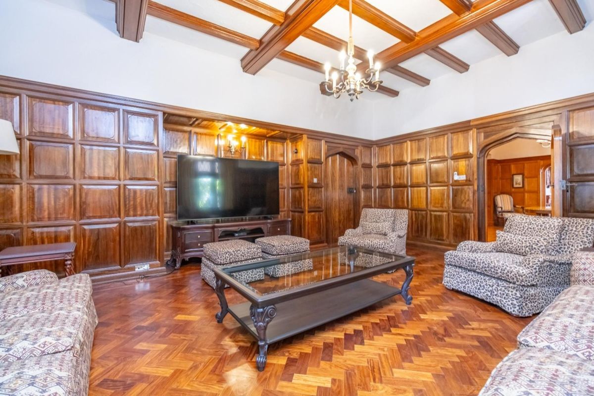 A classic living room featuring rich wood wall paneling, intricate herringbone parquet flooring, and a decorative beamed ceiling with a traditional chandelier.