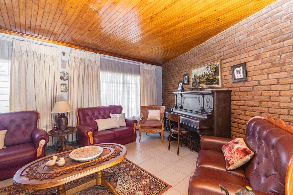 A living room featuring a rustic exposed brick wall, tiled flooring, and a traditional wood-paneled ceiling.