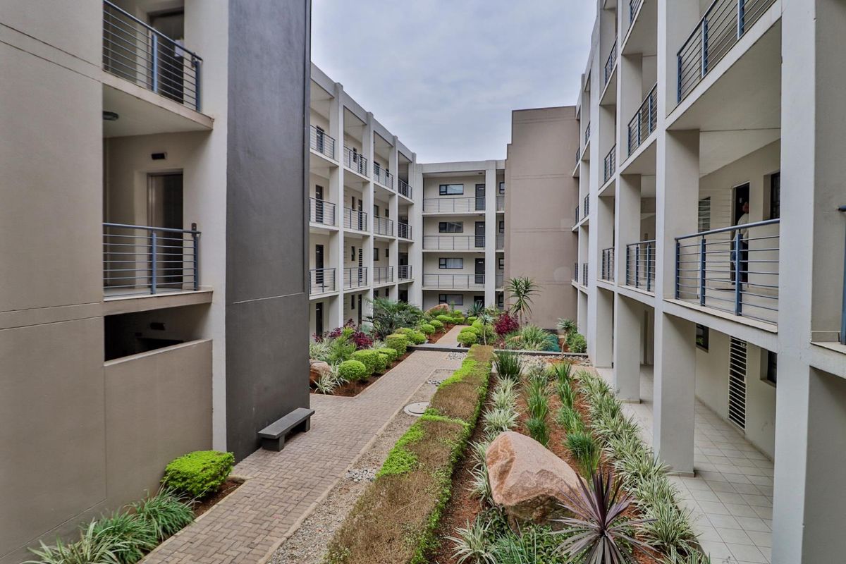 A view of the apartment complex courtyard featuring landscaped garden beds, paved walkways, and multi-level balconies with metal railings.
