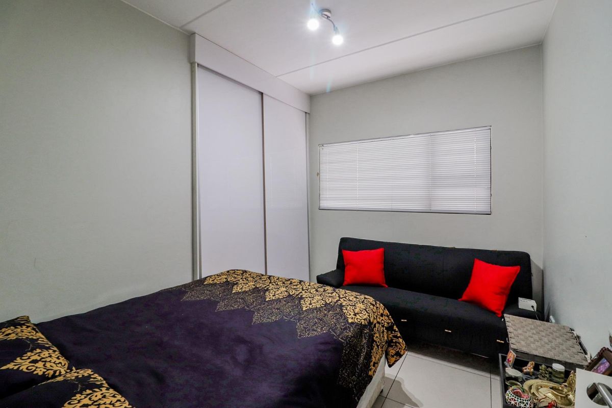 A functional bedroom featuring built-in sliding door cupboards, tiled flooring, and a horizontal window with fitted blinds.