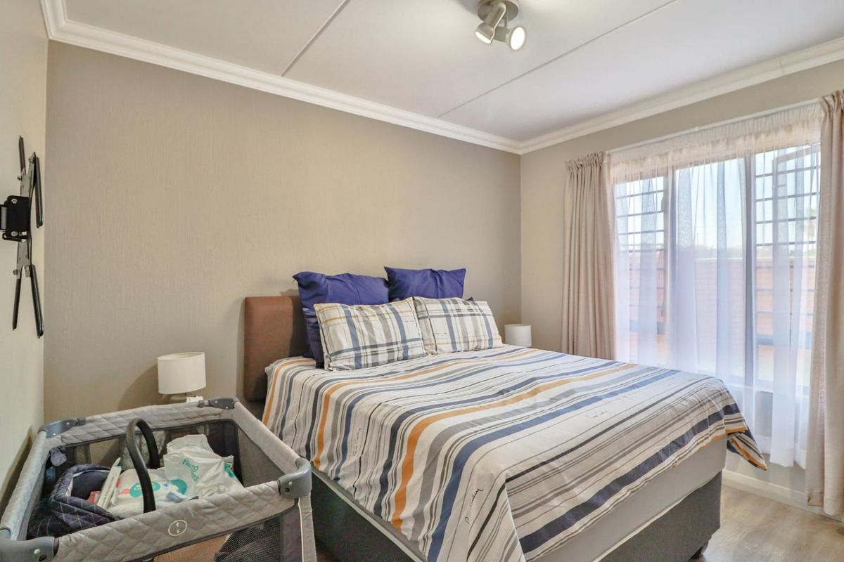 A well-lit bedroom featuring neutral wall tones, crown molding, and a large window with curtain tracks, providing a comfortable living space.