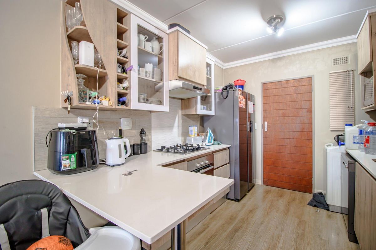 Functional kitchen featuring light wood-tone cabinetry, stone-look countertops, built-in gas hob, oven, and extractor fan with wood-look flooring.