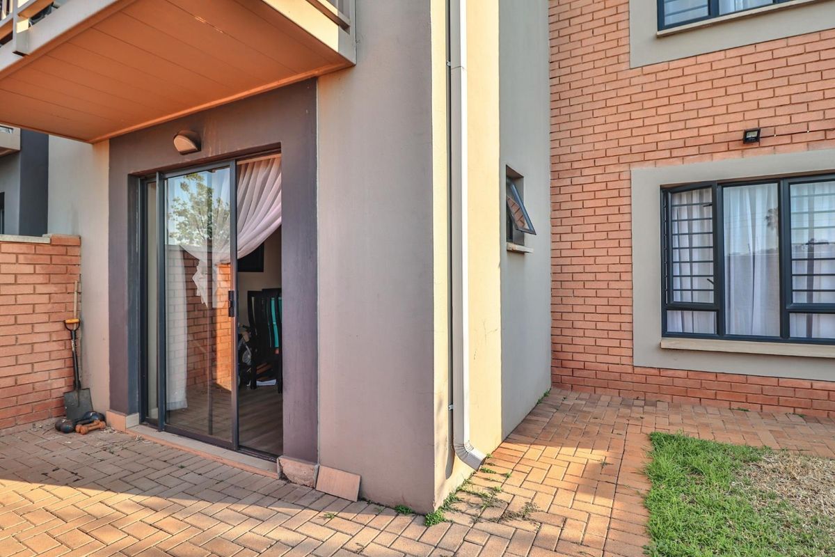 Rear view of the townhouse featuring a paved patio area, sliding glass door access, and brick facade with security bars on windows.