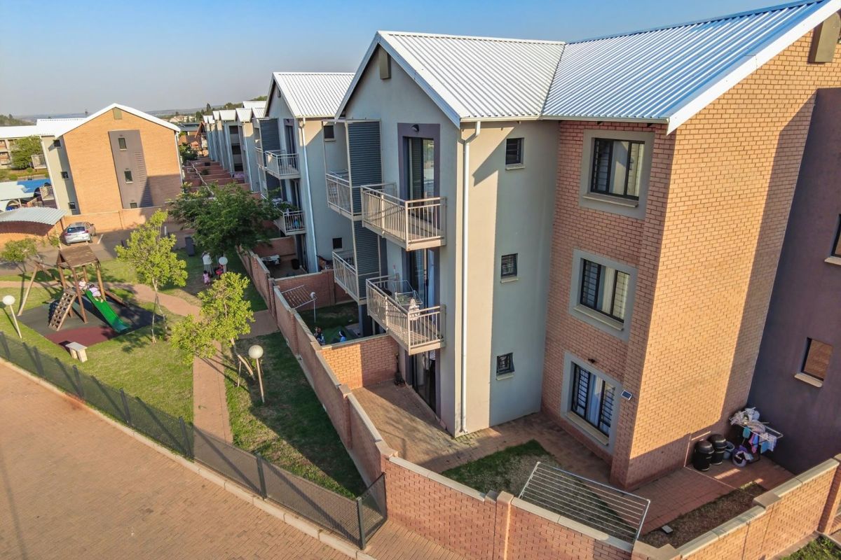Aerial view of a townhouse complex featuring multi-story brick buildings with metal roofing, private balconies, and shared landscaped garden areas.