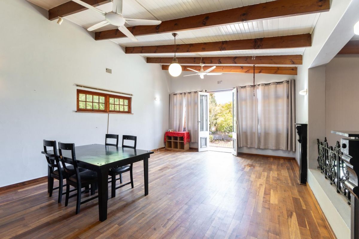 Spacious living area featuring exposed timber ceiling beams, wooden flooring, and direct access to an outdoor patio through double doors.