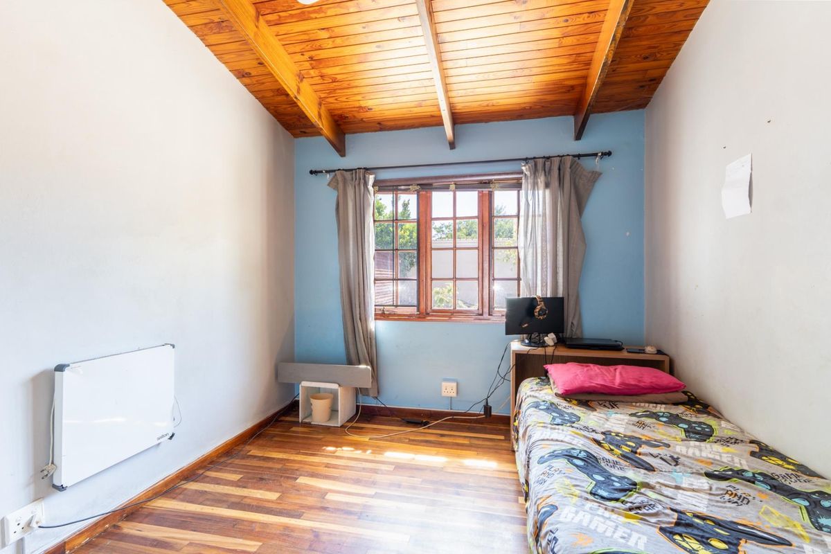 A bedroom featuring exposed timber ceiling beams, wooden window frames, and timber flooring, equipped with a wall-mounted heater.