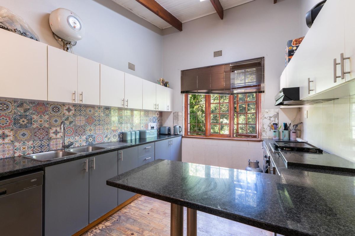 A functional kitchen featuring granite countertops, two-tone cabinetry, a decorative tiled backsplash, and a breakfast bar, with exposed timber ceiling beams.