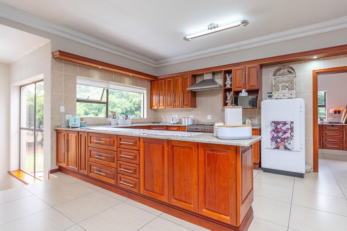 Spacious kitchen featuring warm-toned wooden cabinetry, stone countertops, a built-in stove with extractor fan, and tiled flooring throughout.