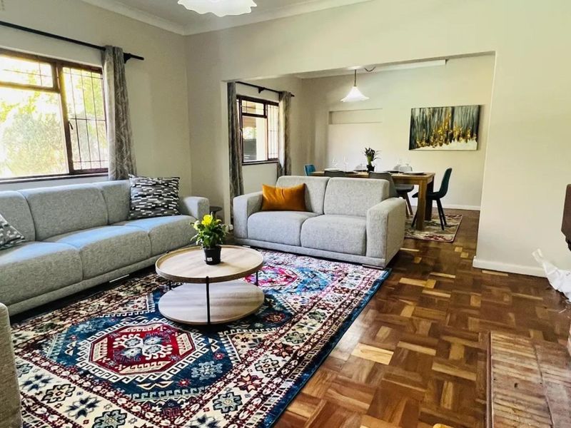 Spacious open-plan living and dining area featuring classic parquet flooring, a brick fireplace, and large windows providing ample natural light.