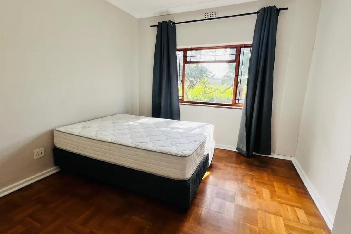A bedroom featuring classic parquet flooring and a timber-framed window with dark curtains.