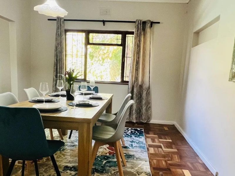 A well-lit dining room featuring classic parquet flooring, a window with security bars, and neutral wall finishes.