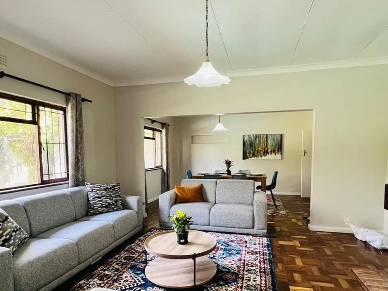 Spacious open-plan living and dining area featuring classic parquet flooring, a brick fireplace, and neutral walls, offering a versatile layout for family living.