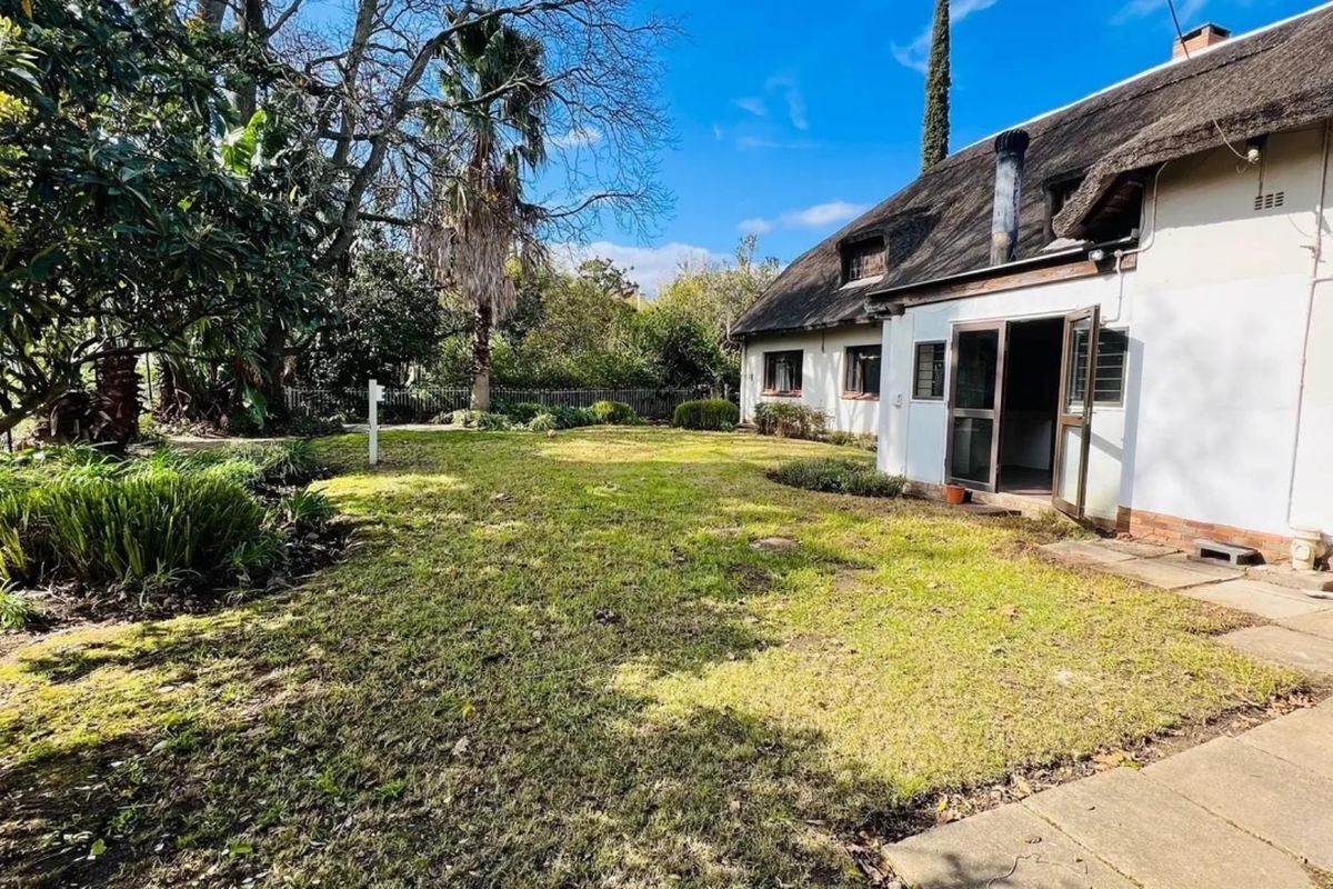 Rear view of a house featuring a traditional thatch roof, chimney, and a spacious garden with a paved walkway.