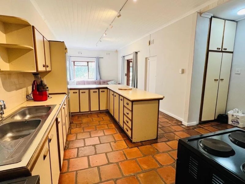 Spacious kitchen featuring terracotta tile flooring, ample built-in cabinetry, a central island, and a double basin sink, offering a functional layout.