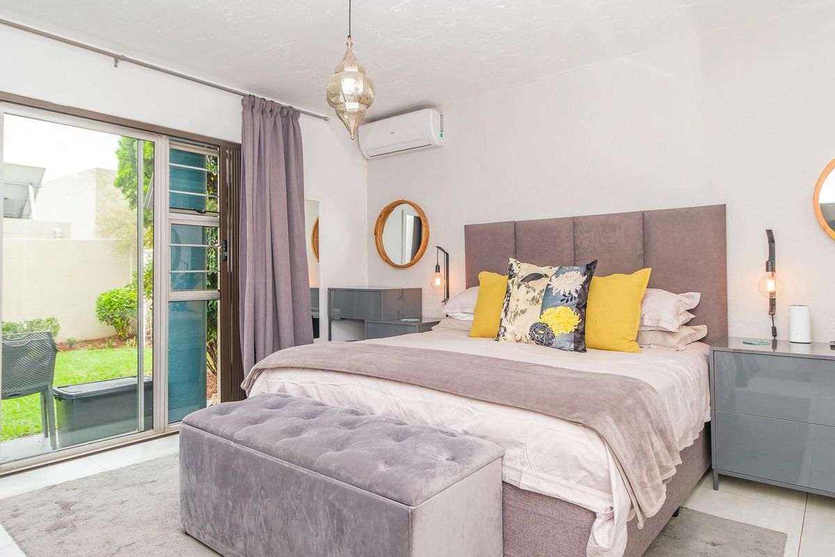 A well-maintained bedroom featuring tiled flooring, a split-system air conditioner, and large sliding glass doors providing direct access to the garden.