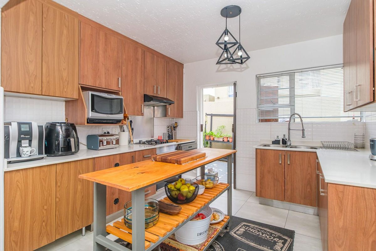 A functional kitchen featuring wood-look cabinetry, a gas hob, built-in microwave, and a central island, with direct access to an outdoor area.