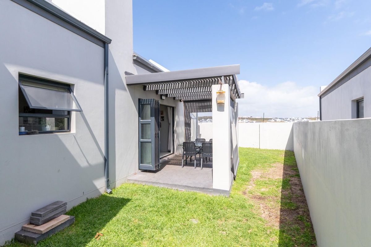 A rear exterior view featuring a covered patio with a pergola, adjacent to a small private garden and enclosed by boundary walls.