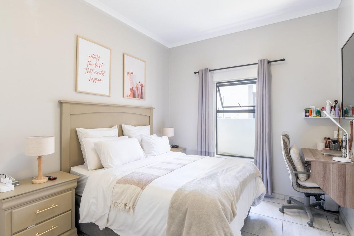A well-lit bedroom featuring neutral tones, tiled flooring, a window with curtain treatments, and a built-in wall-mounted desk area.