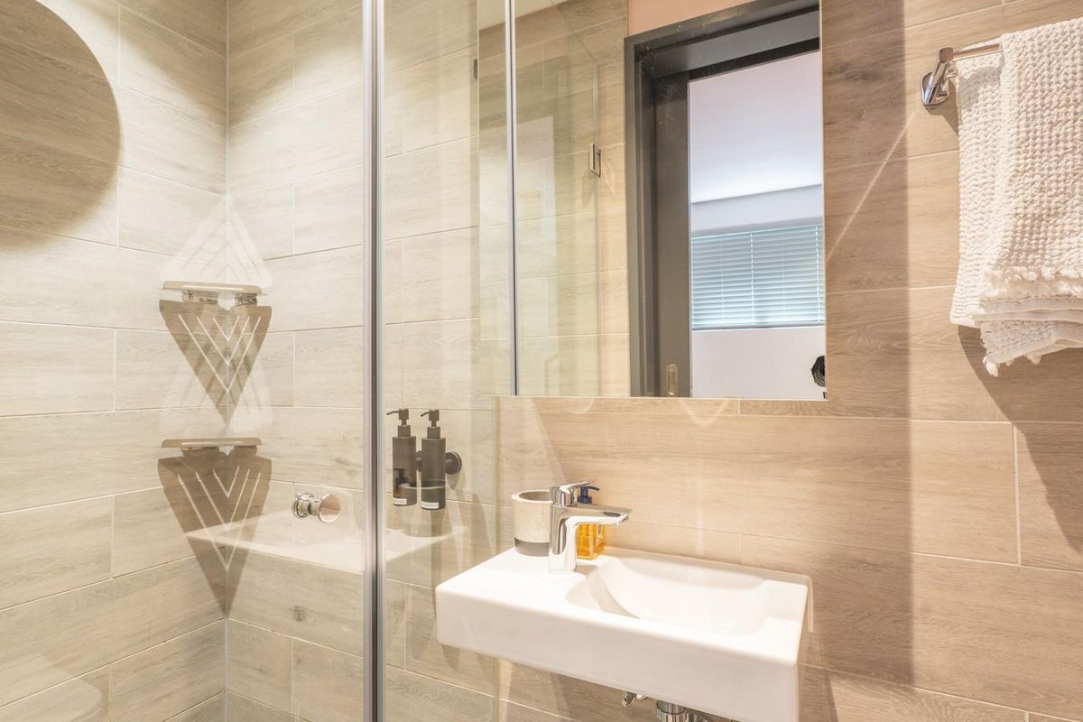 Modern bathroom featuring a wall-mounted basin, glass-enclosed shower with tiled walls, and a sleek mirror, offering a clean and contemporary aesthetic.
