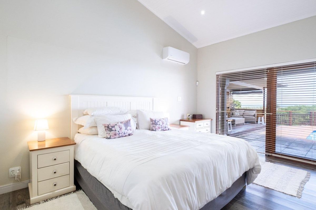 Bright bedroom featuring high vaulted ceilings, a wall-mounted air conditioning unit, and sliding glass doors providing direct access to an outdoor deck and pool area.