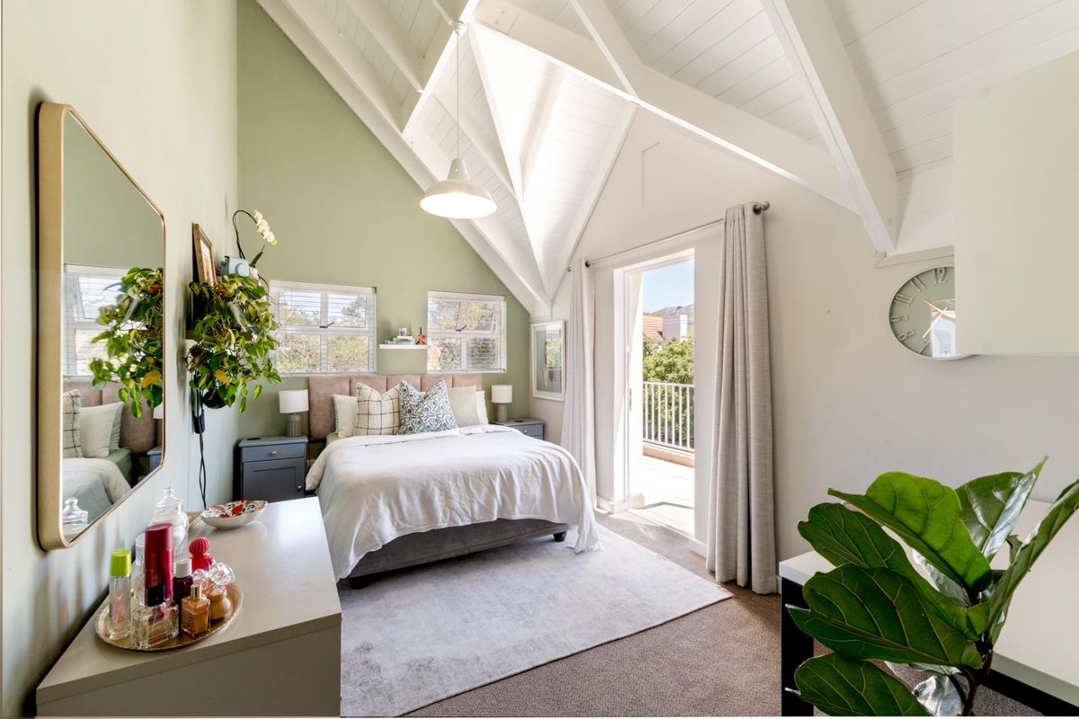 Bright bedroom featuring a high vaulted ceiling with exposed beams, neutral carpeting, and direct access to a private balcony through a glass door.