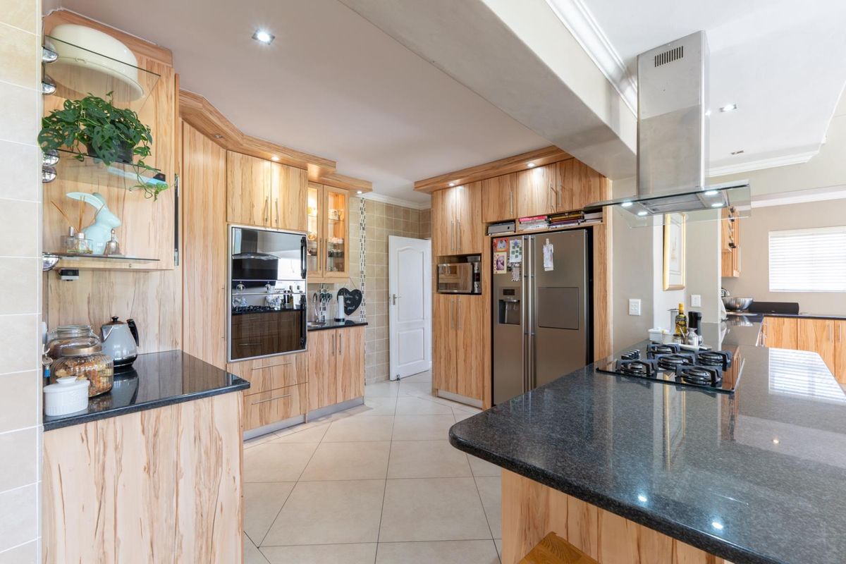 A well-appointed kitchen featuring light wood cabinetry, dark granite countertops, a central island with a gas hob, and integrated stainless steel appliances.