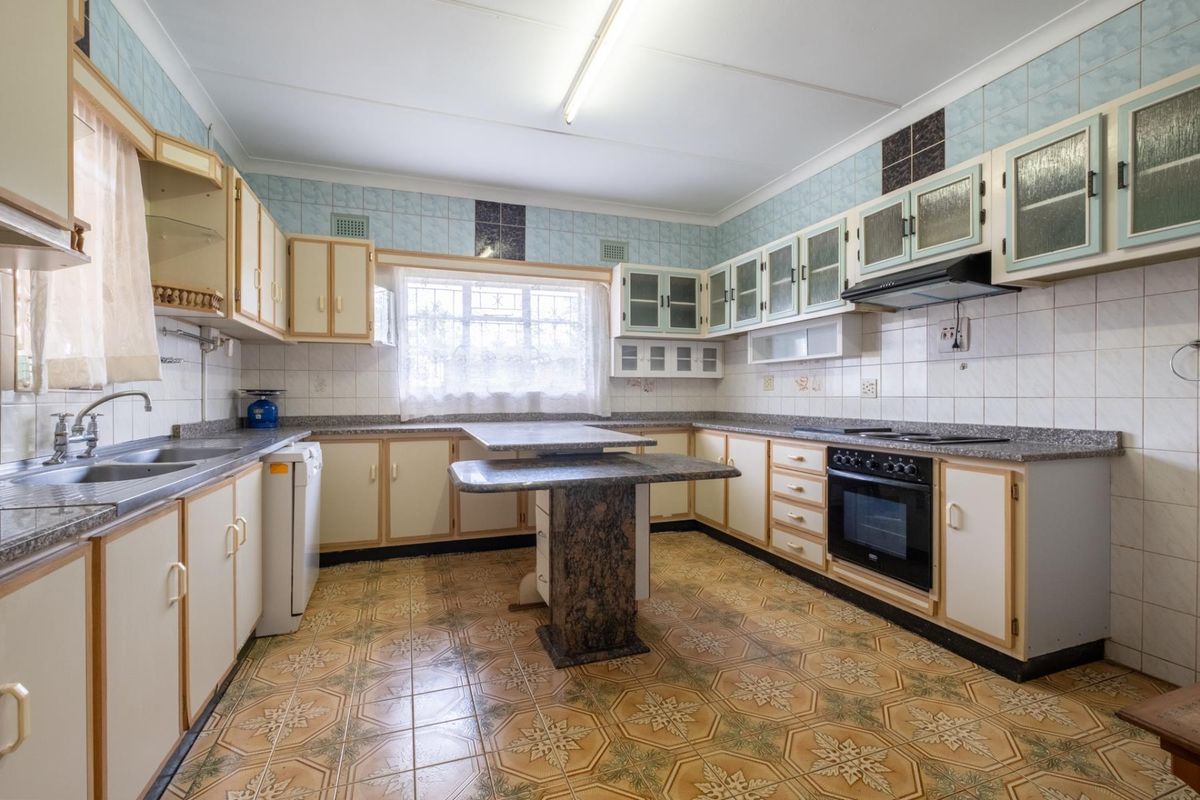 A spacious kitchen featuring built-in cabinetry, a central stone-topped island, integrated oven and hob, and tiled flooring throughout.