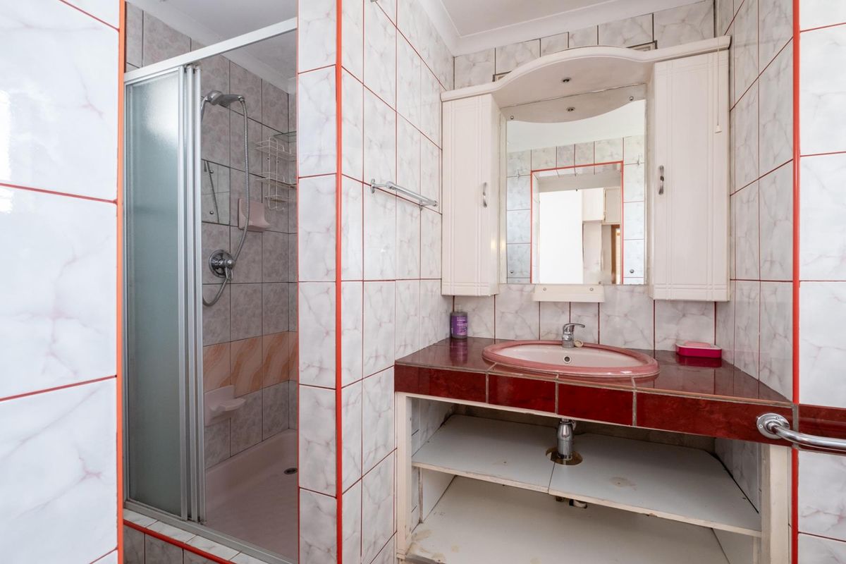 A dated bathroom featuring a shower enclosure, a vanity with a built-in mirror, and tiled walls throughout.