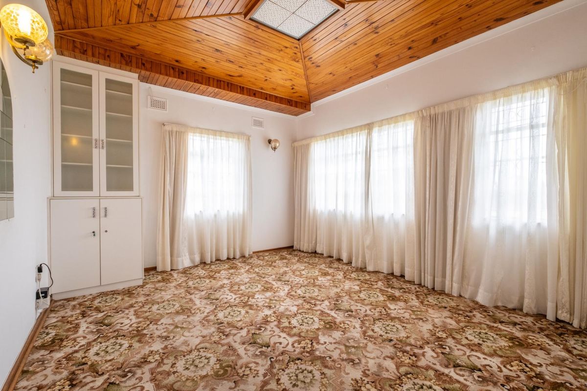 A spacious bedroom featuring a vaulted timber-paneled ceiling, built-in storage cabinetry, and large windows with natural light.