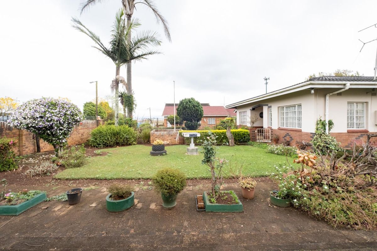 A spacious rear garden featuring a lawn area, established landscaping, and a paved patio section adjacent to the house exterior.