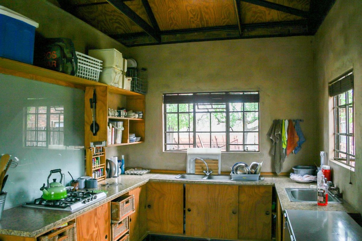 A rustic kitchen featuring wooden cabinetry, a built-in gas hob, double sink, and exposed timber ceiling beams.