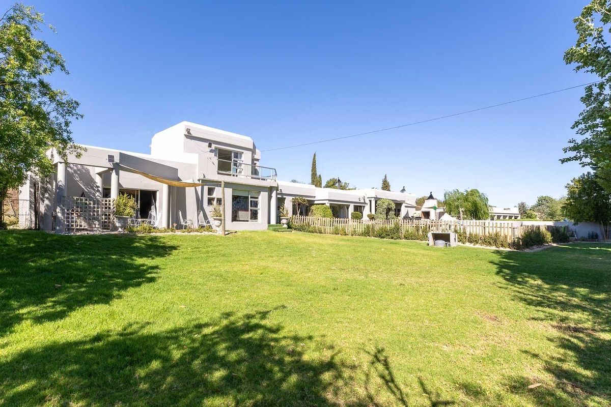 Spacious rear garden view featuring a well-maintained lawn and the rear elevation of the modern farm-style residence with patio areas.