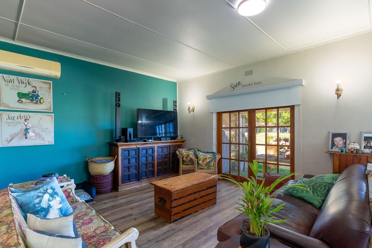 A comfortable living room featuring wood-look flooring, a teal accent wall, and wooden French doors providing direct access to the garden area.