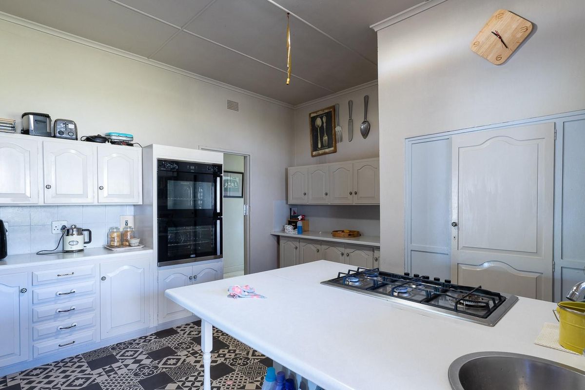A functional kitchen featuring white cabinetry, a built-in double oven, a gas cooktop on a central island, and patterned floor tiles.