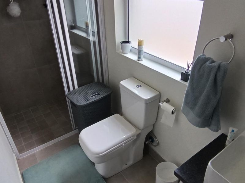 A modern bathroom featuring a glass-enclosed shower, a white toilet, and a vanity basin with a sleek mixer tap.