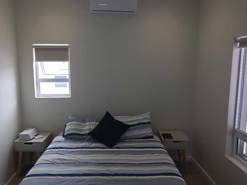 A clean and well-maintained bedroom featuring neutral walls, a split-system air conditioner, and large windows with fitted roller blinds.