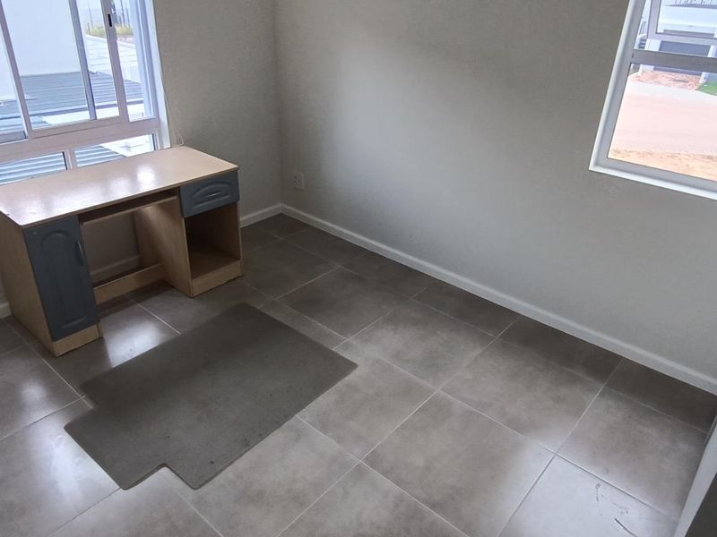 A bright, empty bedroom featuring neutral tiled flooring and large aluminium-framed windows, offering a clean and versatile space ready for personalization.