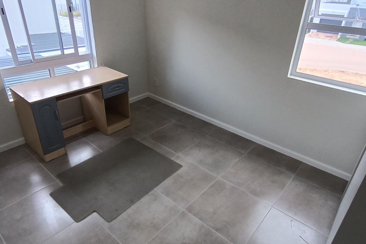 A bright, empty bedroom featuring neutral tiled flooring and large aluminium-framed windows, offering a clean and versatile space ready for personalization.