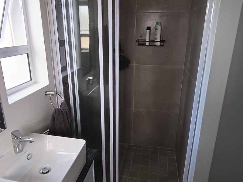 Modern bathroom featuring a tiled shower enclosure, vanity basin with mixer tap, and neutral wall tiling.