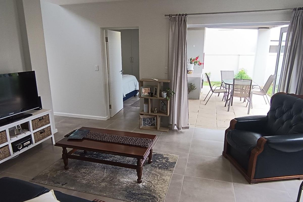 A bright living room featuring large format floor tiles and a sliding glass door providing direct access to an outdoor patio area.