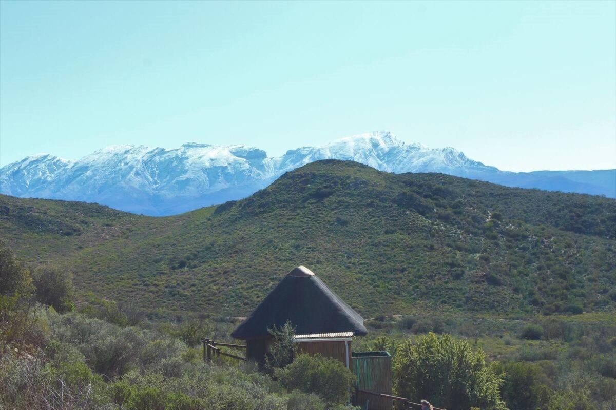 A scenic landscape view featuring a small structure with a traditional thatch roof set against a backdrop of snow-capped mountains.