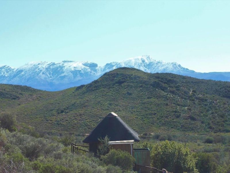 A scenic landscape view featuring a small structure with a traditional thatch roof set against a backdrop of snow-capped mountains.