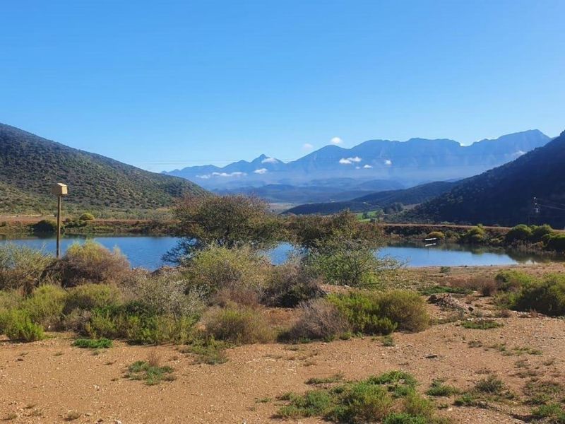 A scenic view of a farm dam set against a backdrop of rolling mountains and clear blue skies.