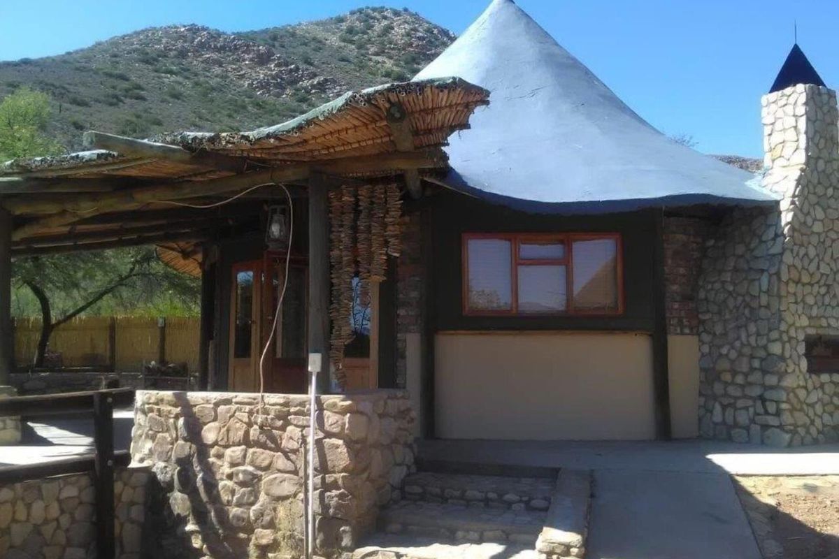 A rustic farm-style dwelling featuring stone cladding, a distinctive conical thatched roof, and an integrated stone chimney with a covered patio area.