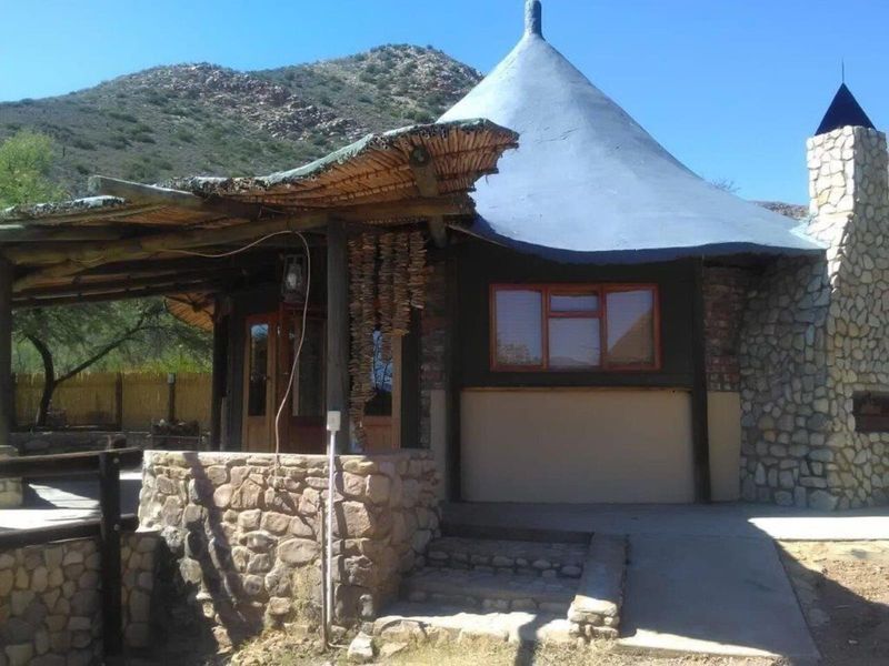 A rustic farm-style dwelling featuring stone cladding, a distinctive conical thatched roof, and an integrated stone chimney with a covered patio area.