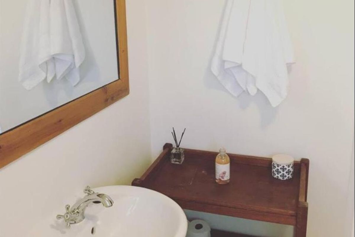 A compact bathroom featuring a white pedestal basin with chrome faucet, a wooden-framed mirror, and wall-mounted storage hooks.