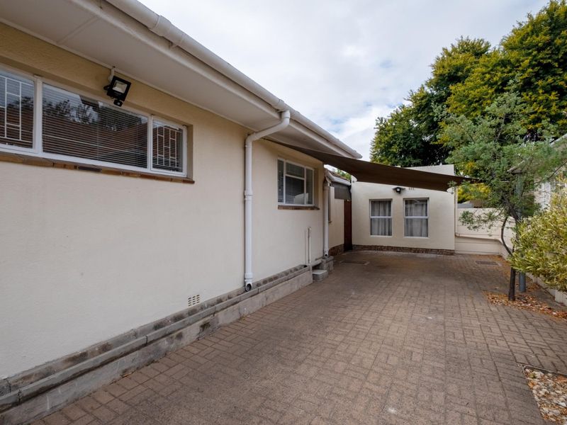 A paved rear exterior area featuring a shade sail, security bars on windows, and functional guttering systems.