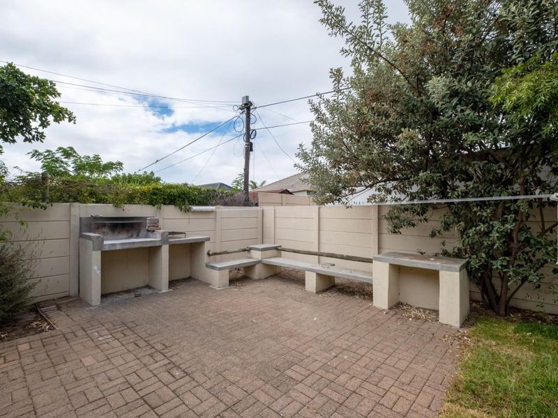 Rear outdoor entertainment area featuring a paved patio, built-in braai, and integrated concrete bench seating against a private boundary wall.