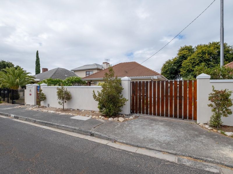 Front exterior view of the property featuring a secure perimeter wall, timber slat gate, and concrete driveway access from the street.